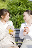 公園のベンチで飲み物を飲む2人の女性
